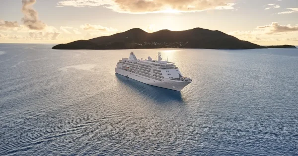 Silversea luxury cruise ship sailing into the sunset with lush tropical islands on the horizon